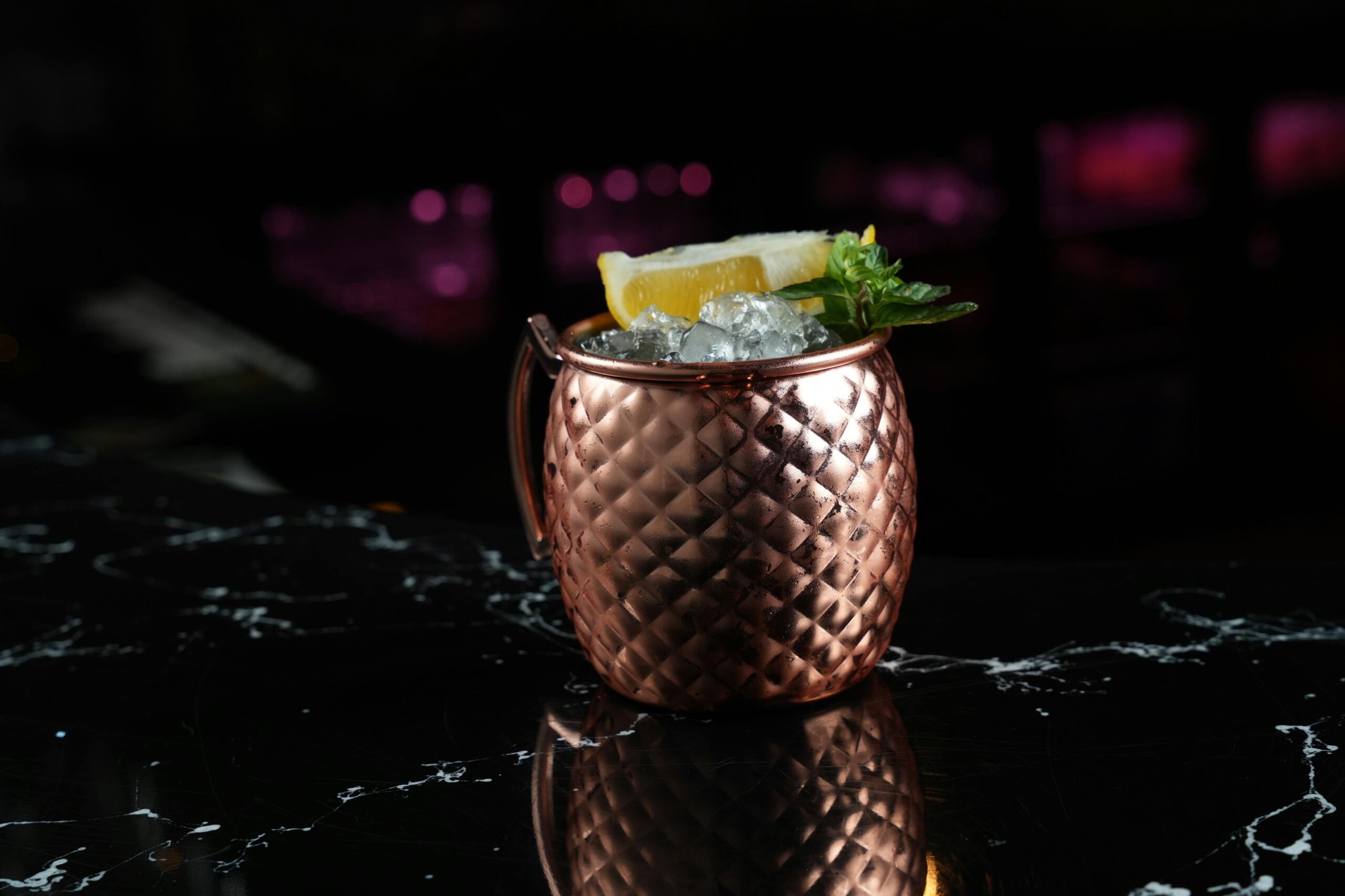 Carte Elegant cocktail in a copper mug with ice garnish on a sleek marble bar counter.